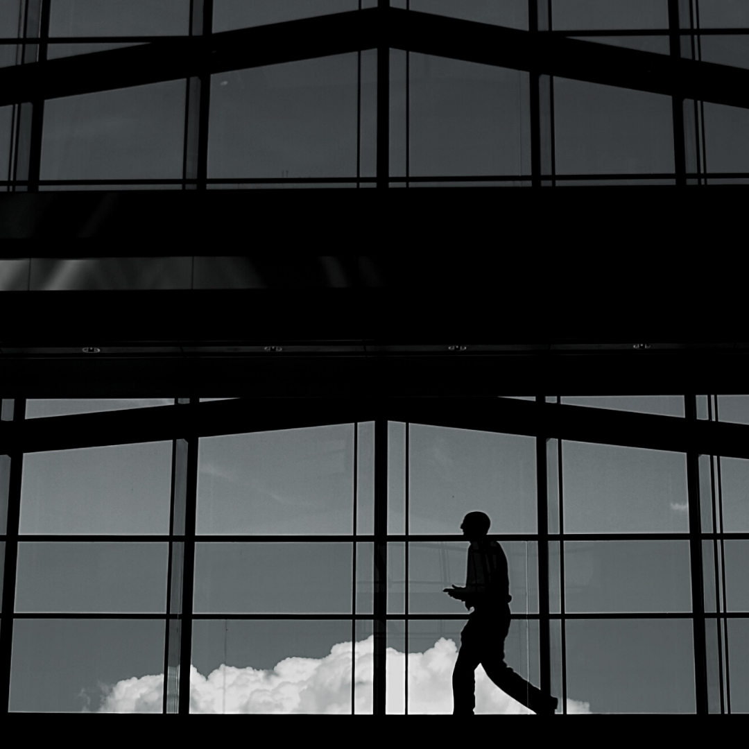 A silhouetted person walking past a glass fronted building.