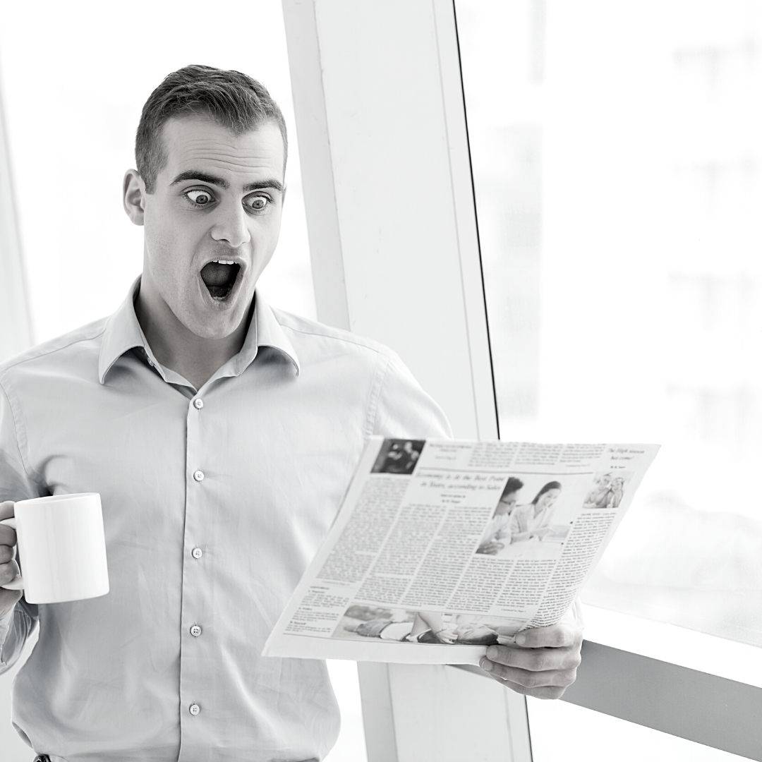 A property consultant  looking surprised as he reads his newspaper. 